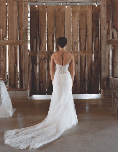 Bride wearing a strapless wedding dress with a long train, standing with her back to the camera.
