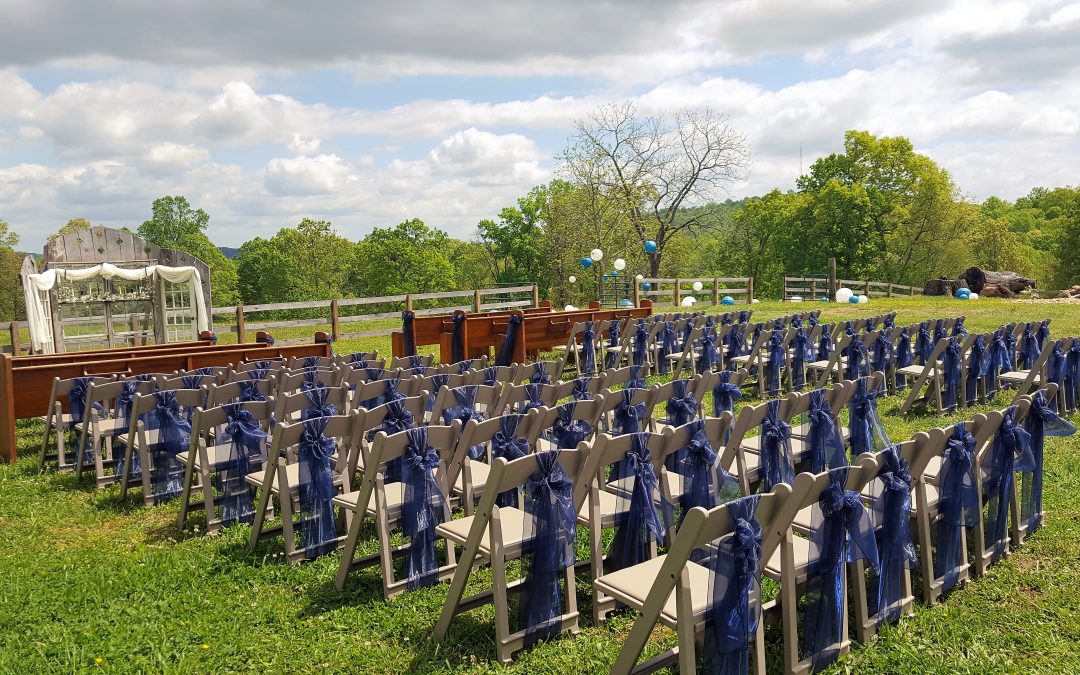 Rows of chairs with blue sashes arranged for an outdoor wedding ceremony.