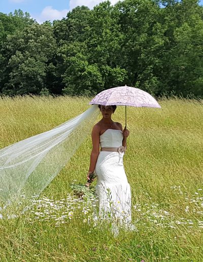 Bride wearing a white dress and holding a pink umbrella in a grassy field.