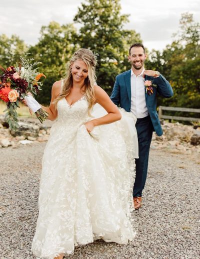 Bride in a white wedding dress holding a bouquet, walking with a groom in a blue suit.
