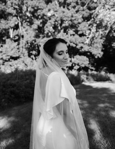 Bride wearing a wedding dress and veil, standing outdoors with a serene expression.