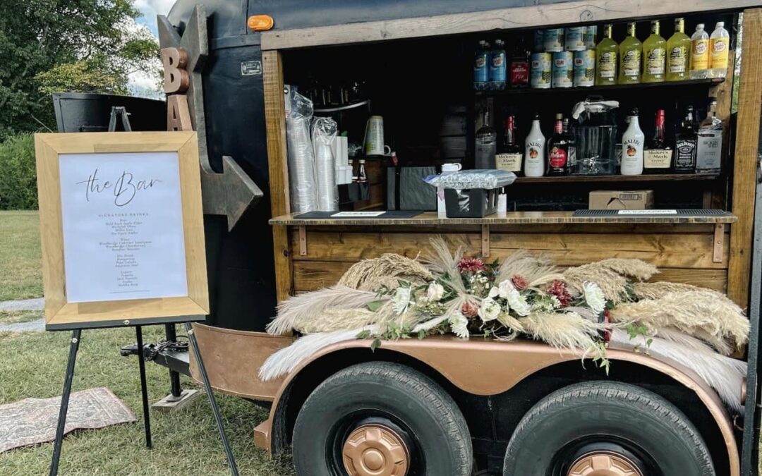 Mobile bar trailer displaying a variety of alcoholic beverages and a menu on an easel.