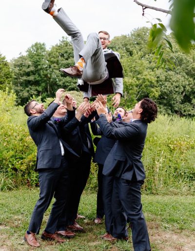 A group of men in suits lifting another man in celebration outdoors.