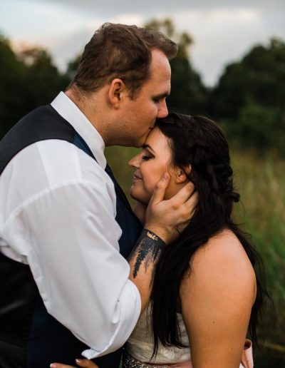 A couple sharing an intimate moment outdoors, with one partner kissing the other's forehead.