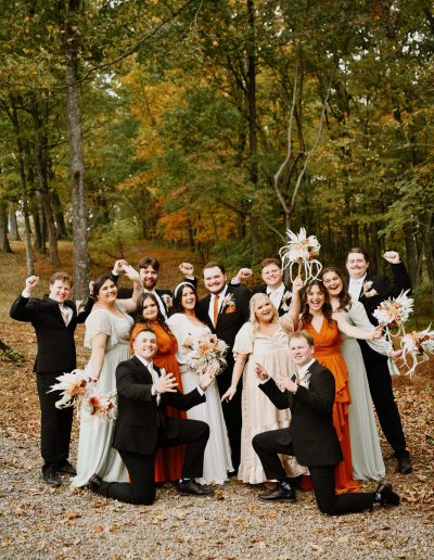 Wedding party posing outdoors in formal attire with floral arrangements in hand.