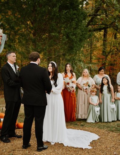Bride in a white dress and groom exchanging vows during an outdoor wedding ceremony surrounded by guests.