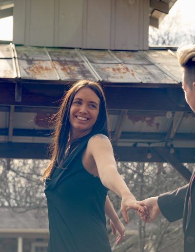 Newlyweds holding hands, with one person smiling and looking at the other, set against a rustic gazebo structure.