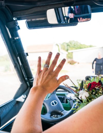 Bride in a vehicle displaying her wedding ring while holding a bouquet of flowers.