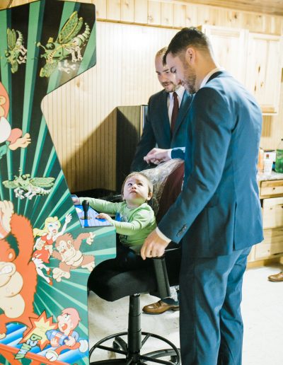 A child sitting at an arcade machine while two adults stand nearby in a casual setting.