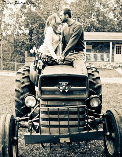 A couple sitting on a vintage tractor, facing each other with smiles, in a black and white photograph.