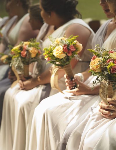 Bridesmaids in white dresses holding flower bouquets during a wedding ceremony.